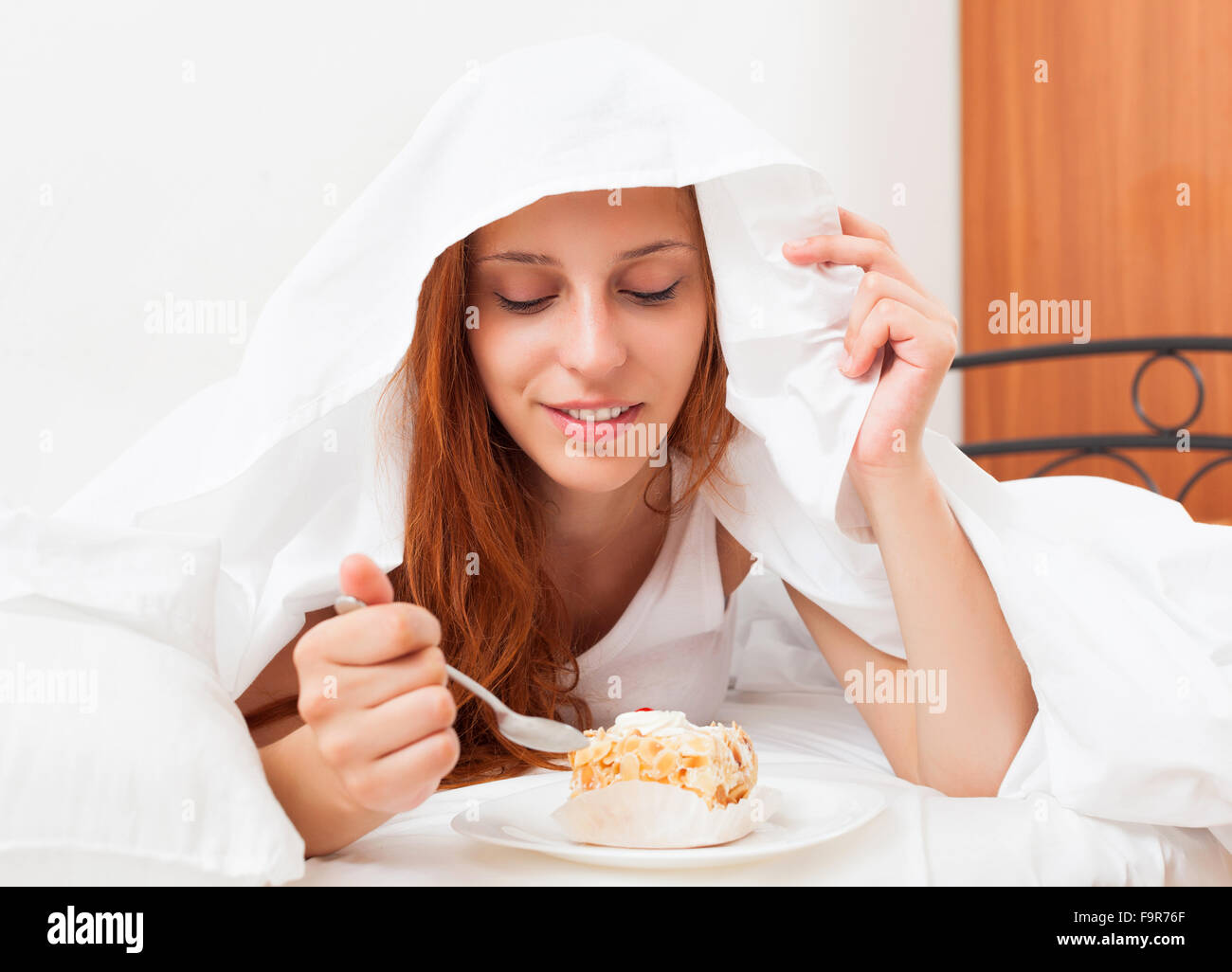 Frau, süße Kuchen unter weißen Laken im Bett Essen Stockfoto