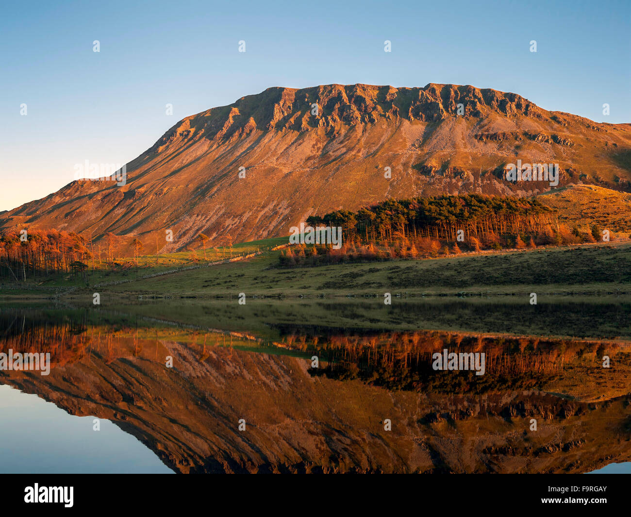 Die steilen Geröll bedeckt Seite von Craig Las liegt in Creggennan See von späten Nachmittag Winter warmes Sonnenlicht beleuchtet reflektierte. Stockfoto