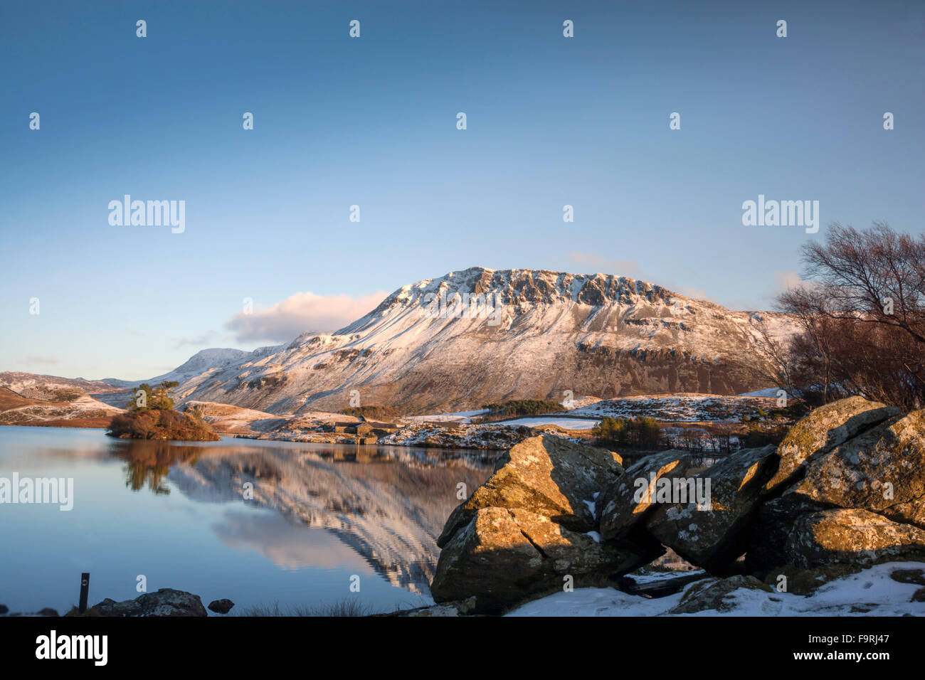 Die Winter tief verschneiten Hänge des Gebirges Cader Idris spiegeln sich im ruhigen Wasser der Cregennen Seen. Stockfoto