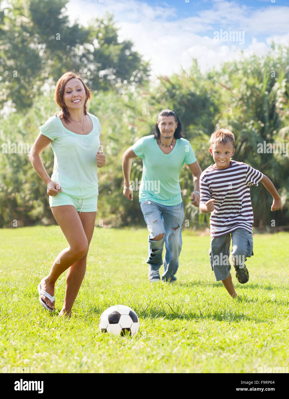Glückliche Eltern mit Teenager-Sohn spielen mit Fußball im Sommerpark Stockfoto