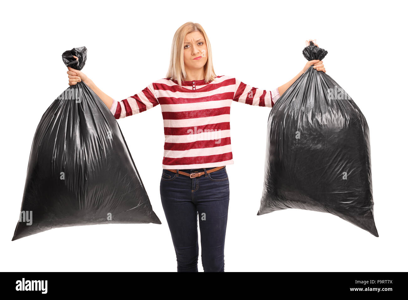 Junge Frau hält zwei schwarzen Müllbeutel und schaut in die Kamera, die isoliert auf weißem Hintergrund verärgert Stockfoto