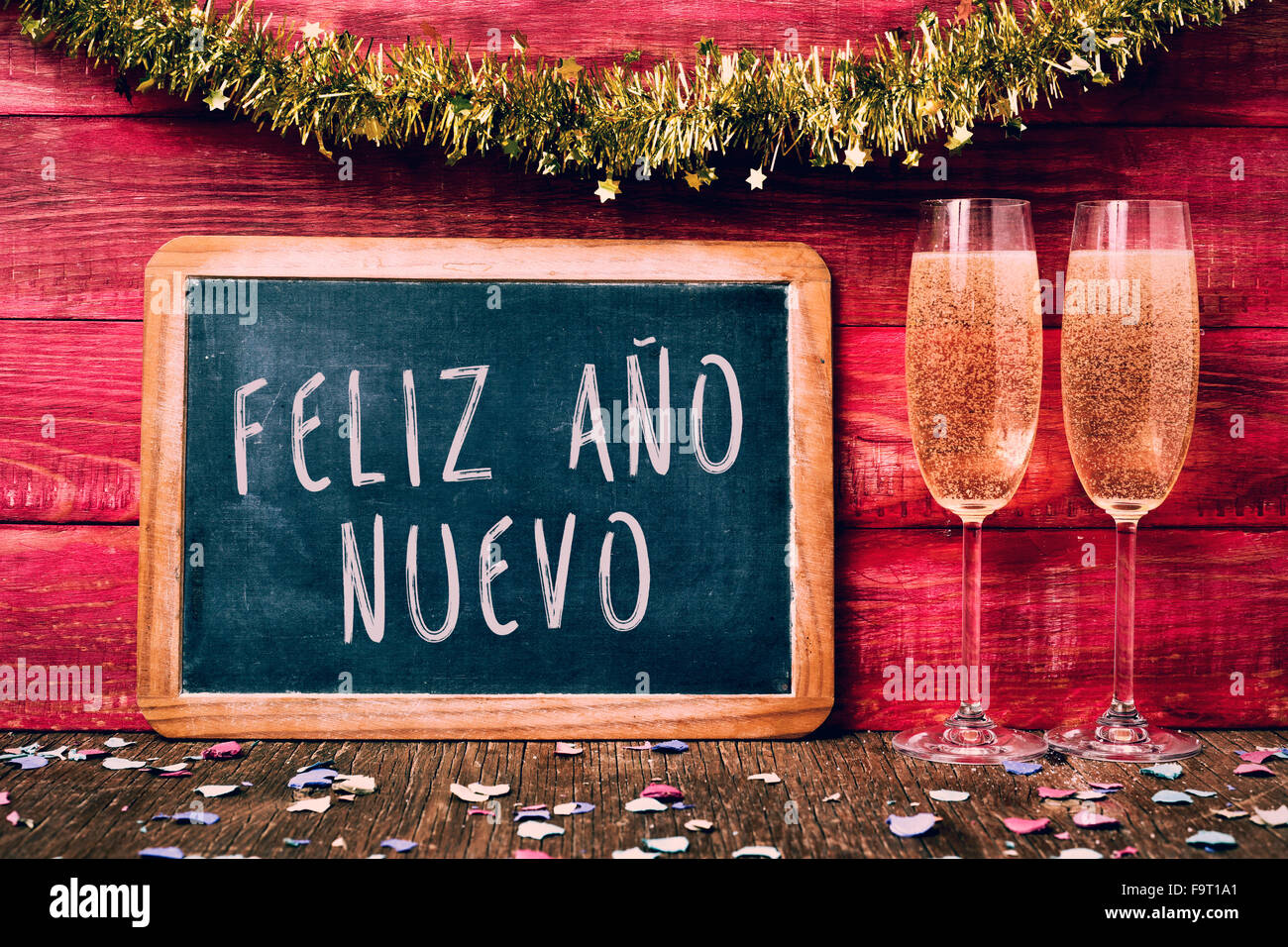 eine Tafel mit dem Text Feliz Ano Nuevo, frohes neues Jahr geschrieben in Spanisch, einige Konfetti und ein paar Gläser mit Sekt Stockfoto