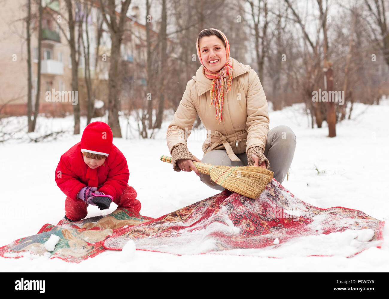 Lächelnde Mutter mit Tochter reinigt Teppich mit Schnee im winter Stockfoto