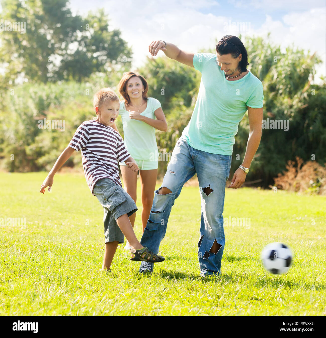 Glückliche Eltern mit Kind spielen mit Fußball im Sommerpark Stockfoto