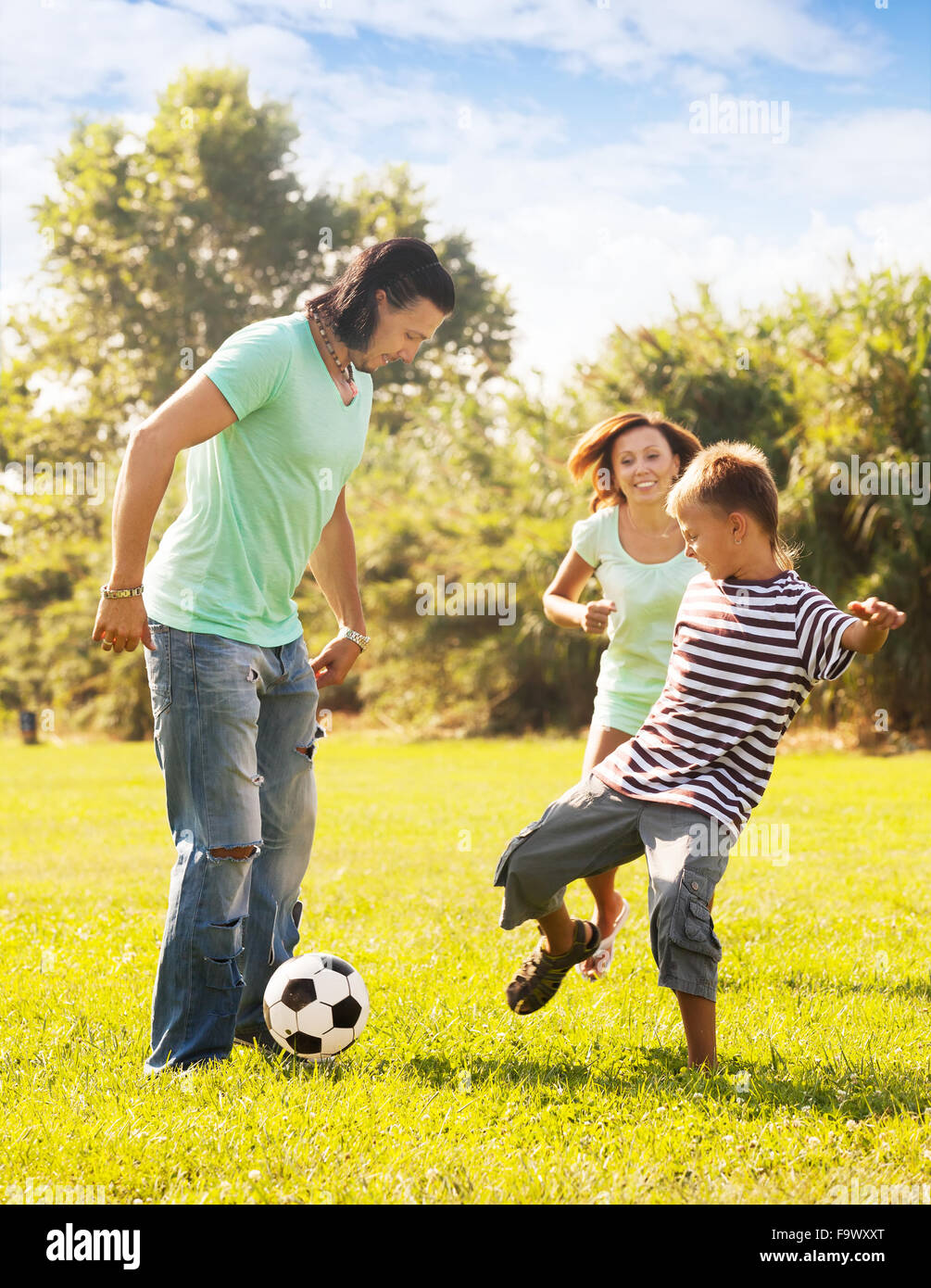 Glückliche Eltern mit Teenager-Sohn spielen mit Fußball im Sommerpark Stockfoto