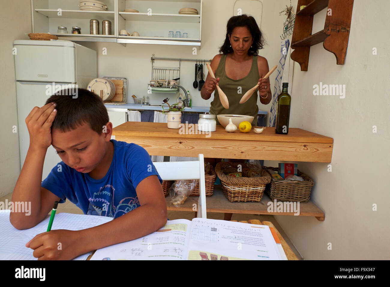 Junge, Hausaufgaben, während seine Mutter kocht. Stockfoto