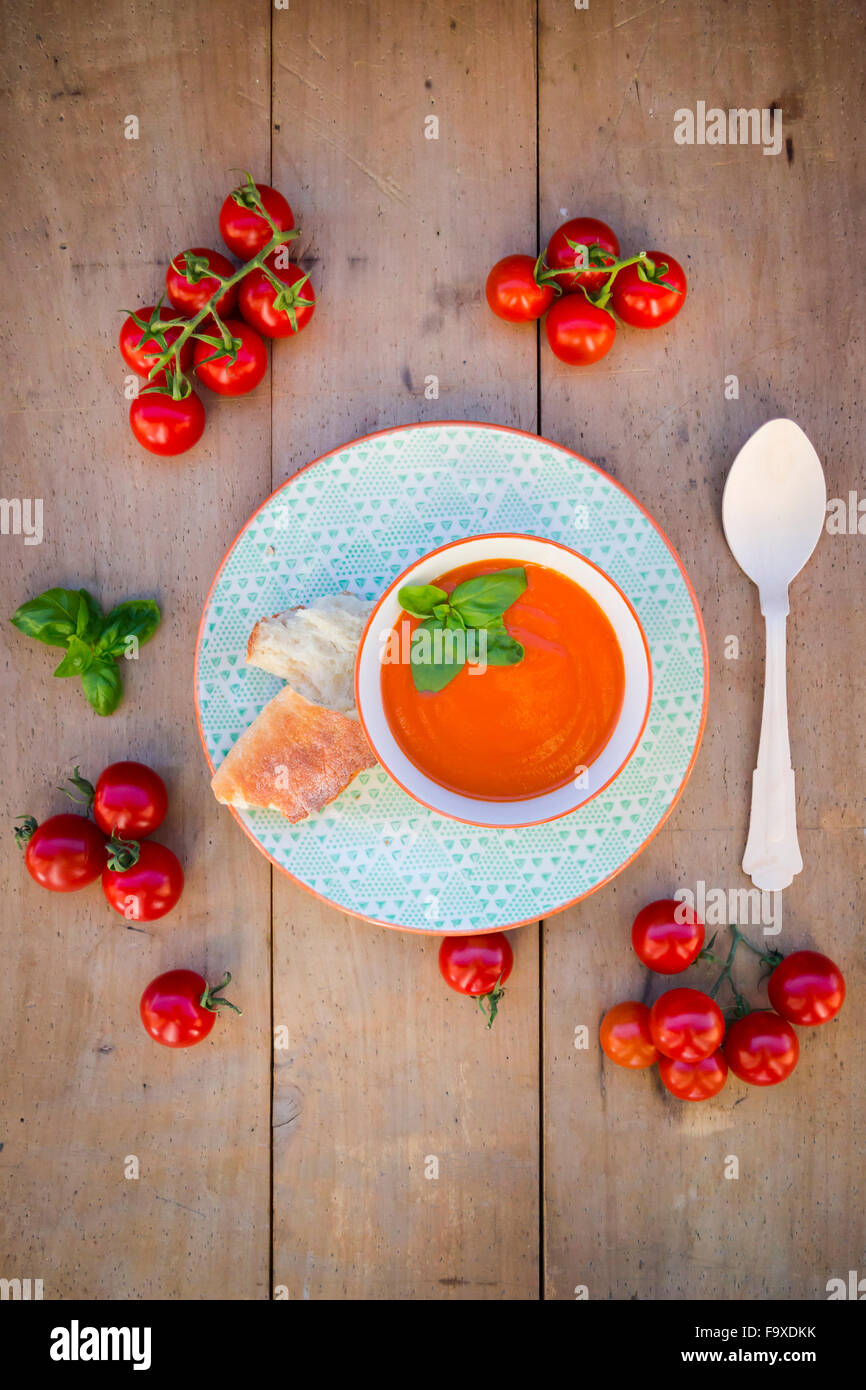Schüssel mit Tomatencremesuppe garniert mit Basilikum und einem recyclebaren Holzlöffel Stockfoto