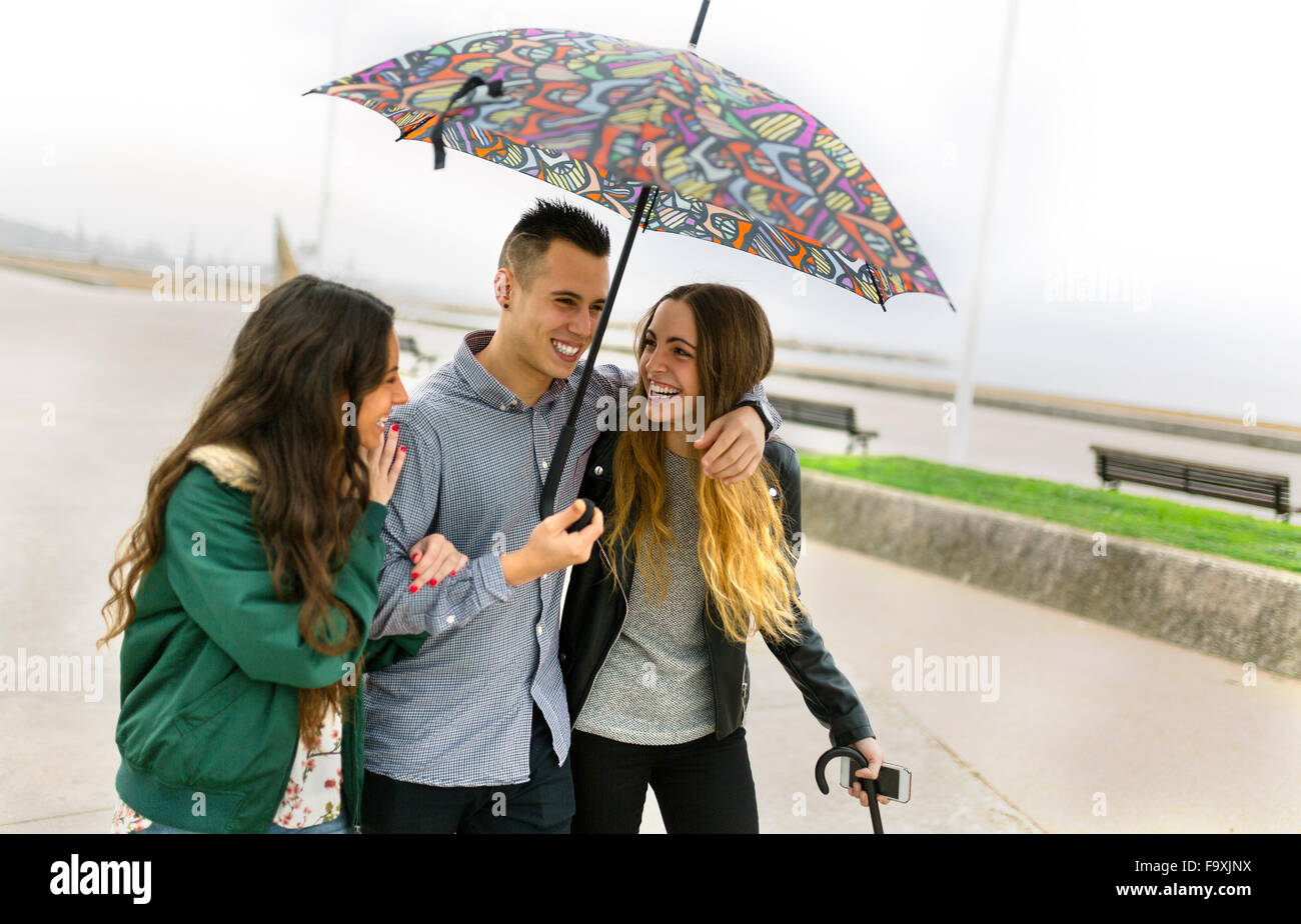 Drei glückliche Freunde auf der Straße mit Regenschirm Stockfoto
