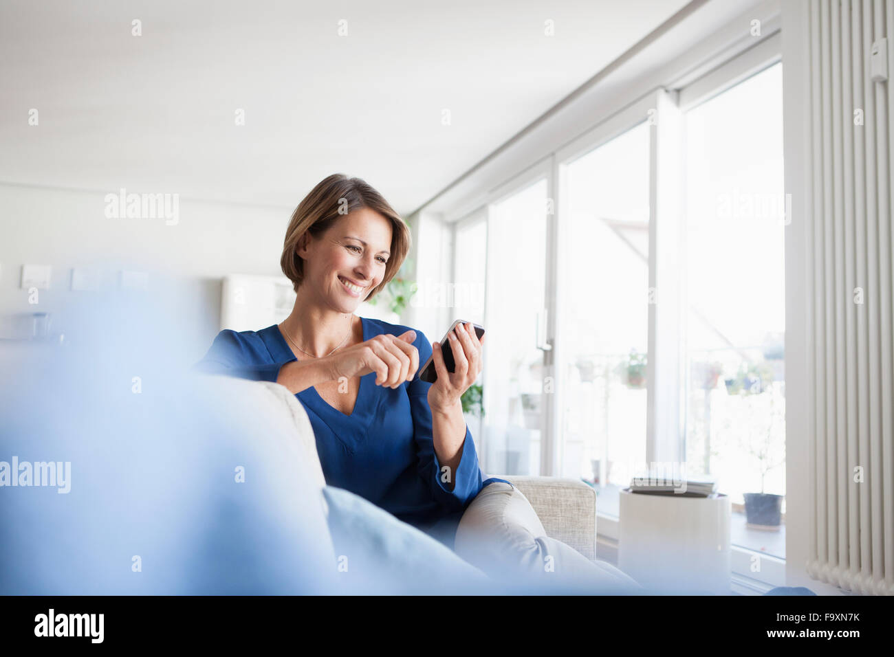 Lächelnde Frau zu Hause sitzen auf Couch Blick auf Handy Stockfoto