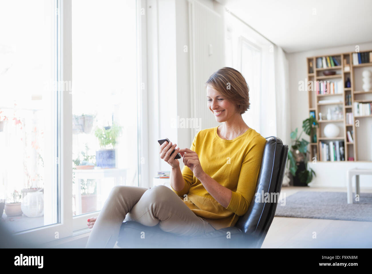 Entspannte Frau zu Hause sitzen auf Ledersessel mit Handy Stockfoto