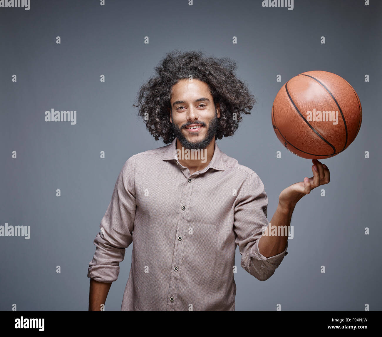 Porträt von lächelnden jungen Mann mit lockigen braunen Haaren einen Basketball auf dem Finger balancieren Stockfoto