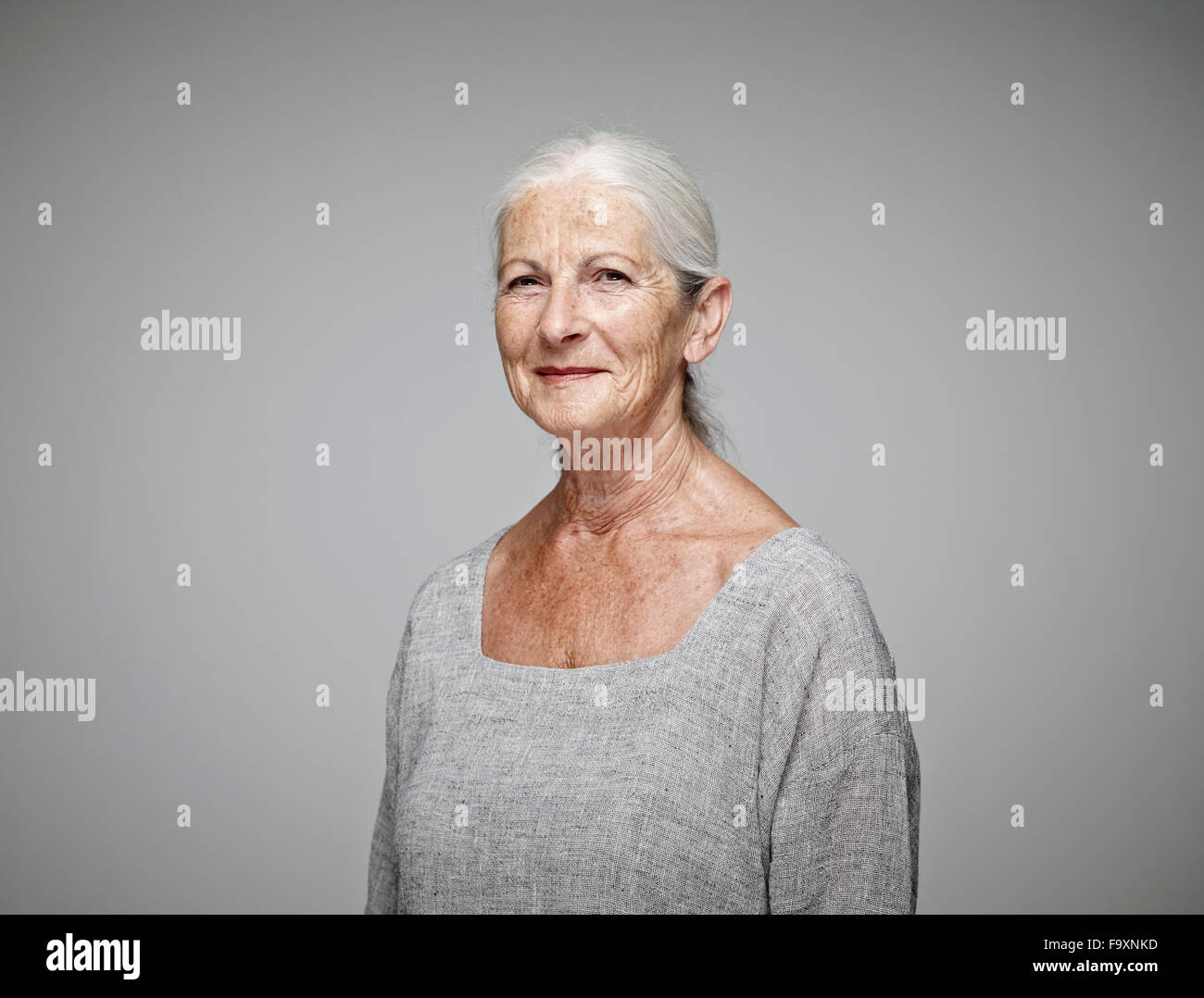 Porträt von lächelnden senior Frau vor grauem Hintergrund Stockfoto