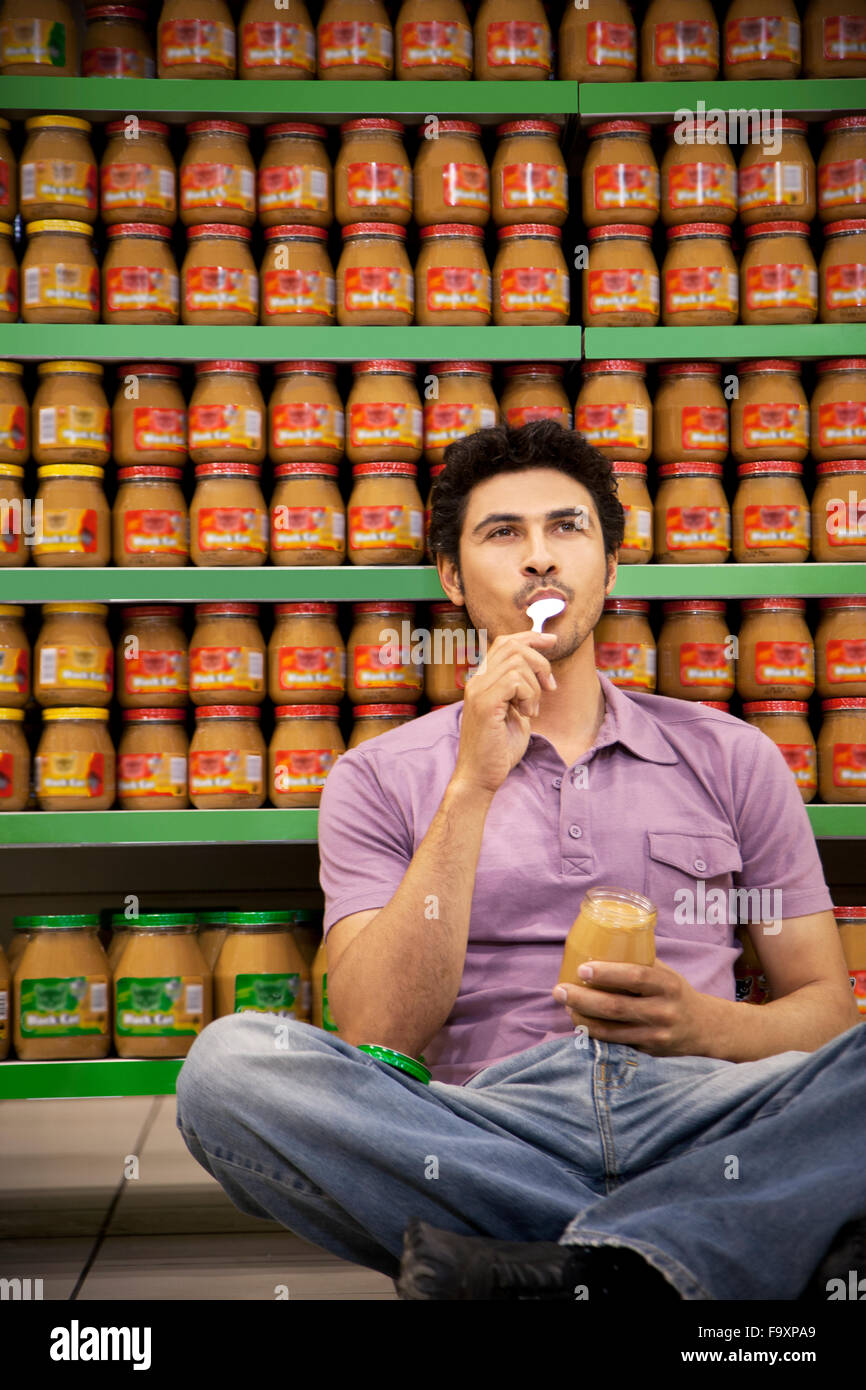 Porträt des Menschen sitzen auf dem Boden eines Supermarktes Probierglas Erdnussbutter Stockfoto