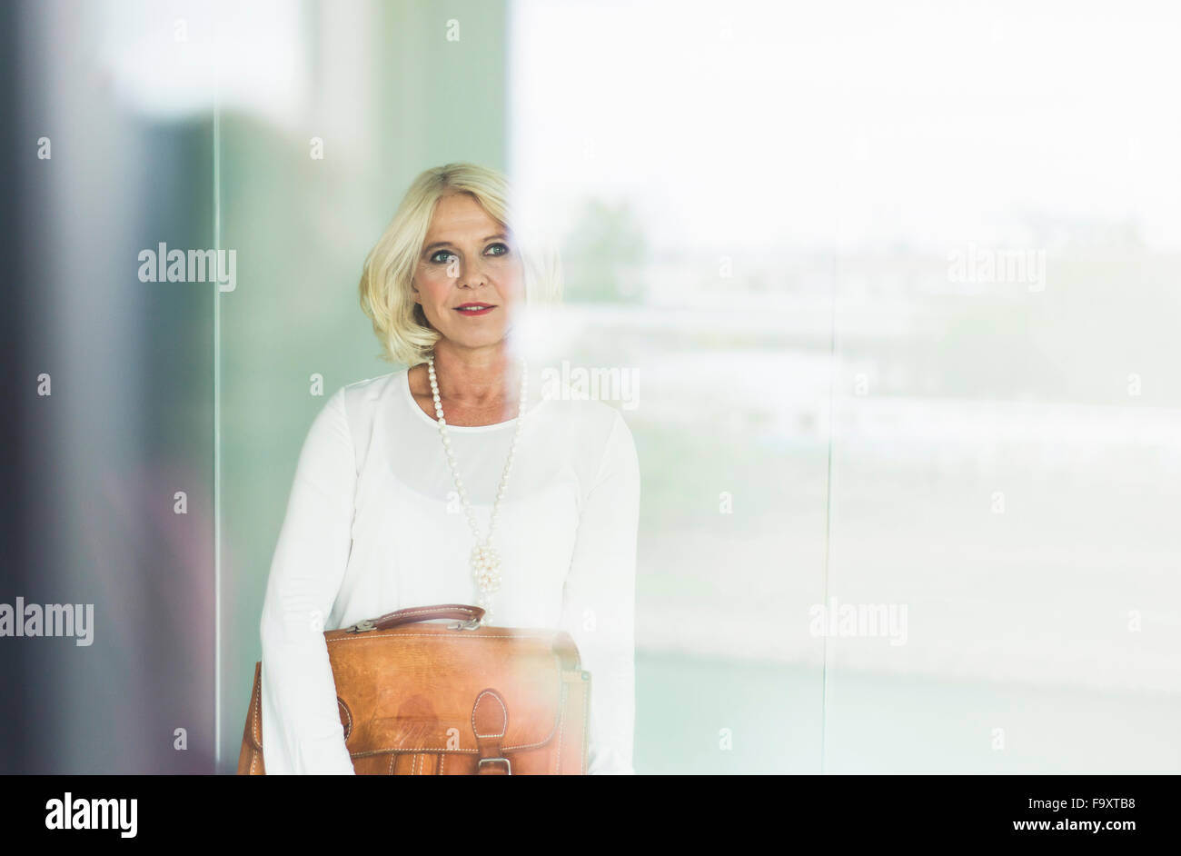 Porträt von nachdenklich Geschäftsfrau mit Ledertasche Blick durch Fenster Stockfoto