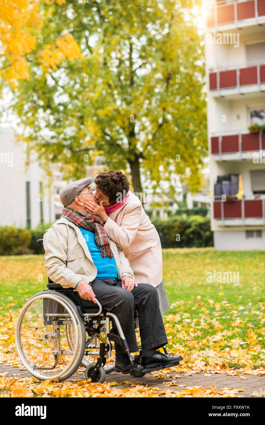 Ältere Frau küssen Mann im Rollstuhl Stockfoto