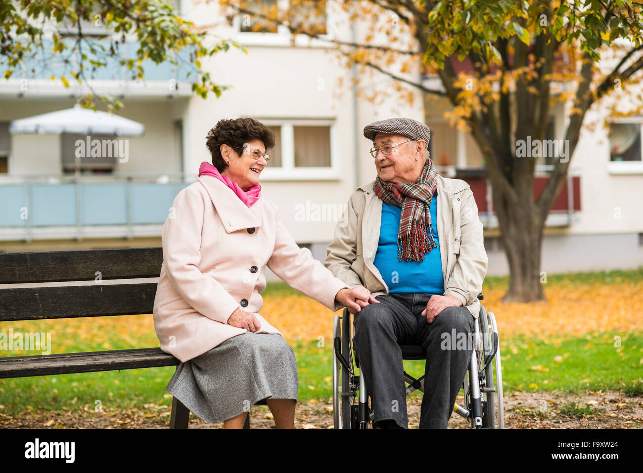 Ältere Frau sitzt neben Mann im Rollstuhl auf Bank Stockfoto