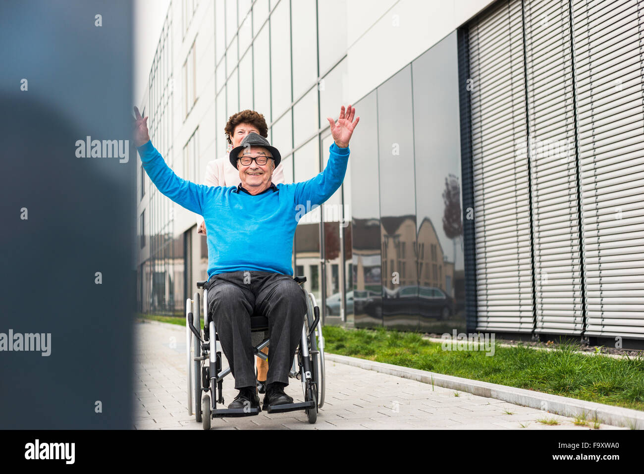Ältere Frau mit jubelnden Mann im Rollstuhl auf Bürgersteig Stockfoto