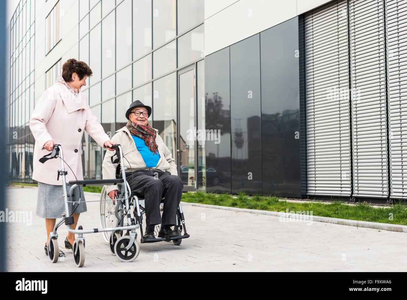 Ältere Frau mit Rädern Walker und senior Mann im Rollstuhl auf Bürgersteig Stockfoto