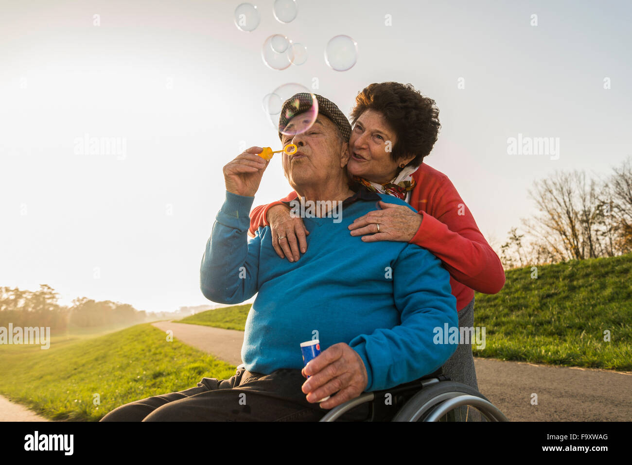 Ältere Frau mit Mann im Rollstuhl bläst Seifenblasen Stockfoto