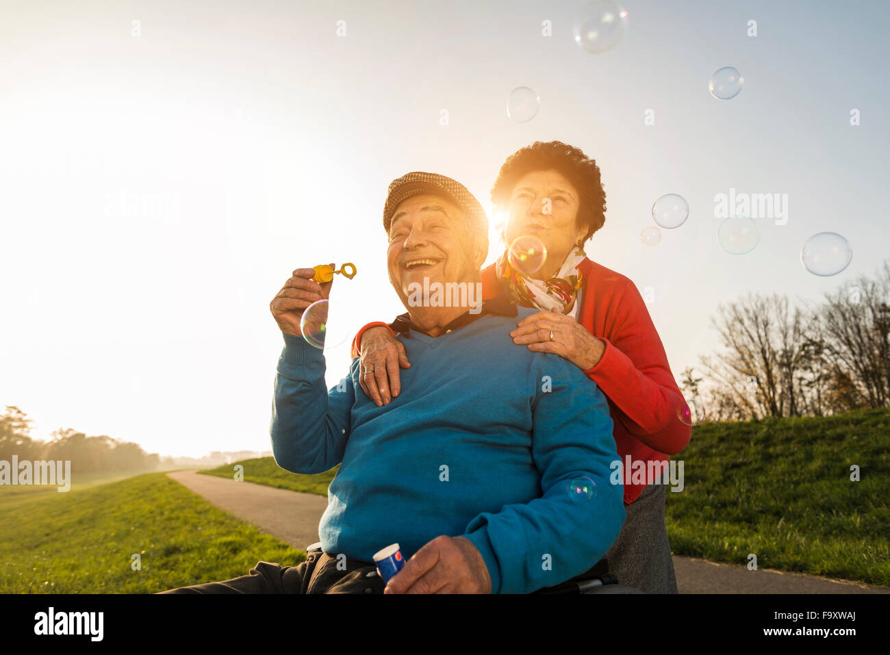 Ältere Frau mit Mann im Rollstuhl bläst Seifenblasen Stockfoto