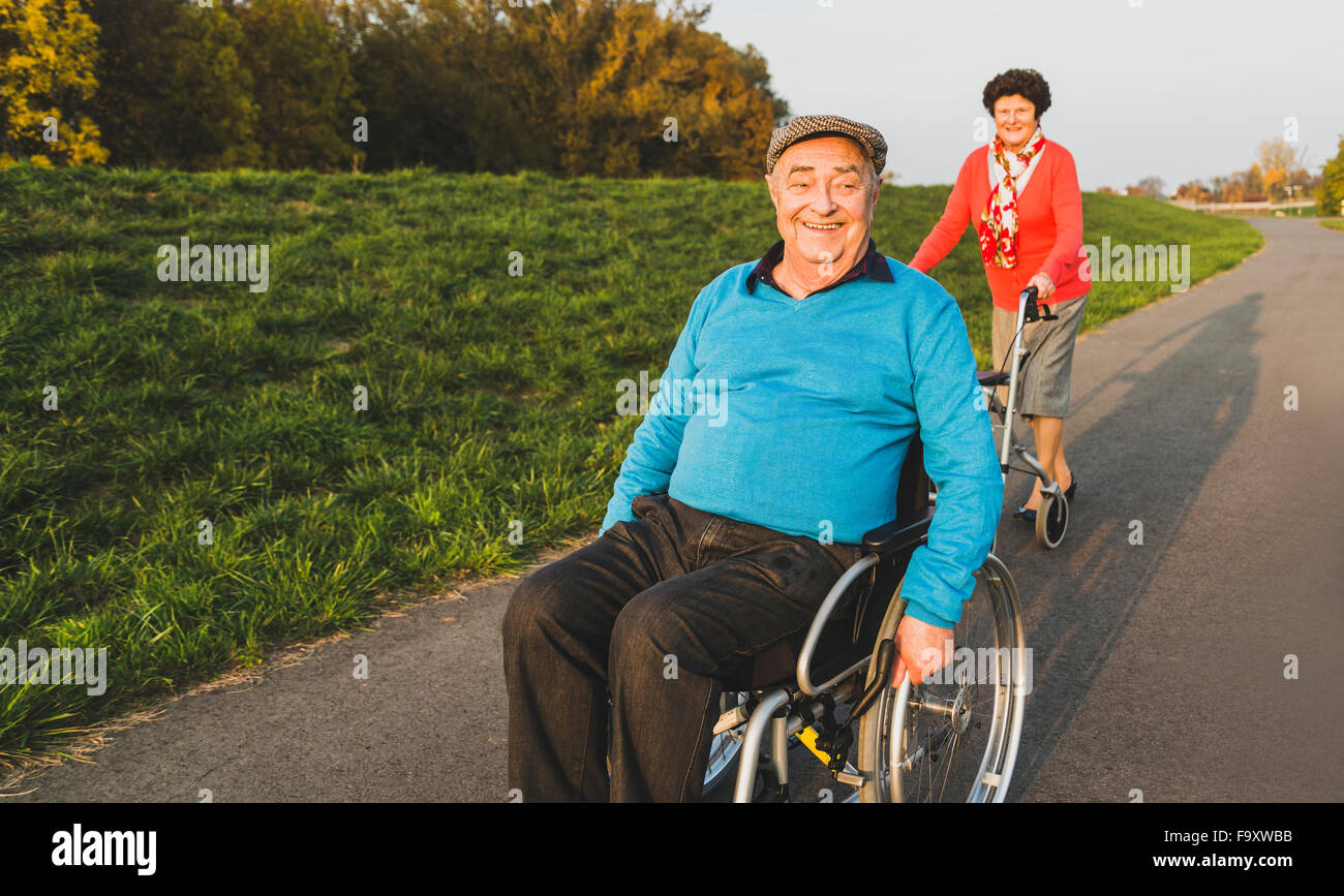 Lächelnd älteres Paar mit Rollstuhl und Rädern Walker auf einem Pfad Stockfoto