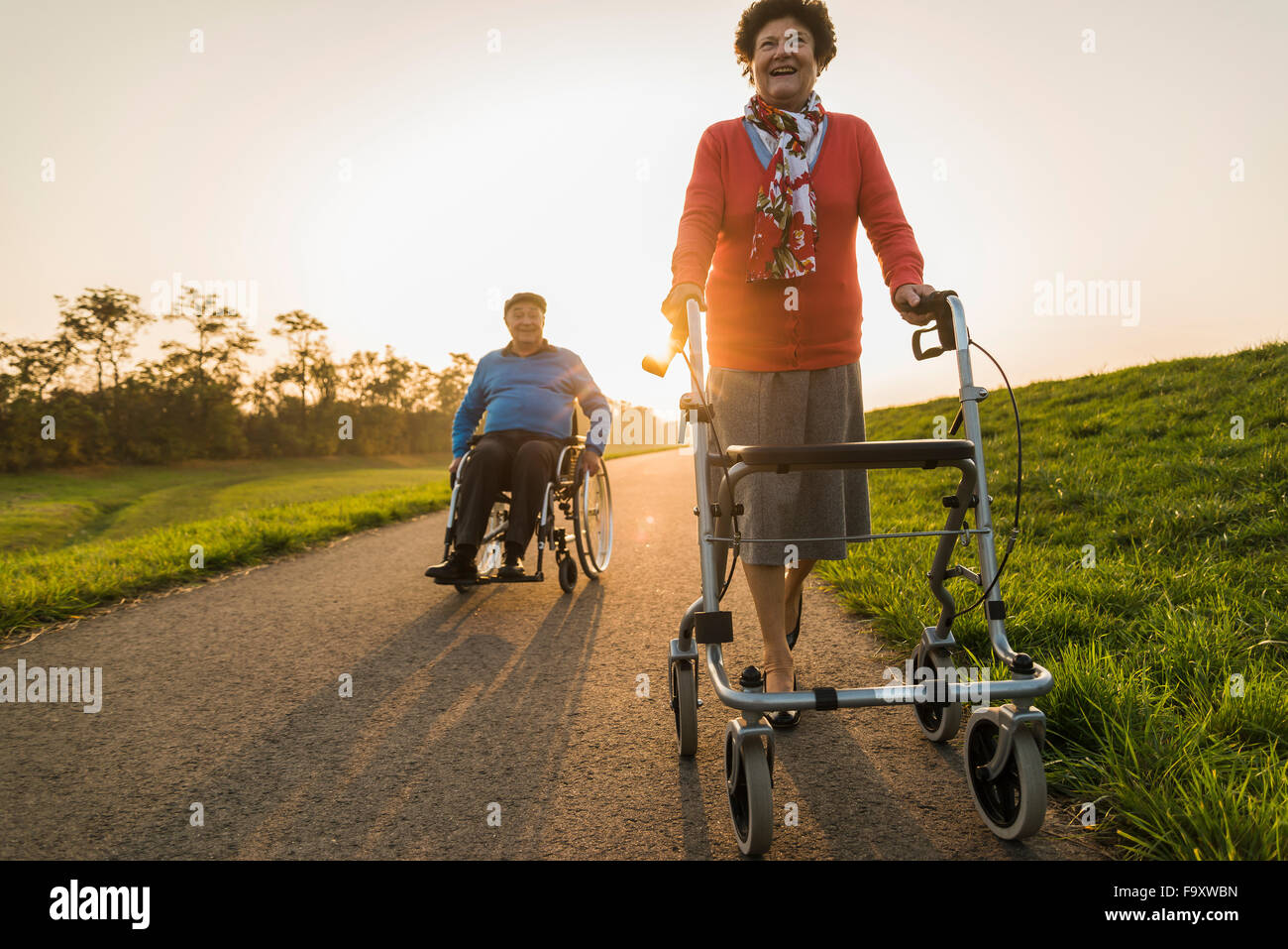Lächelnd älteres Paar mit Rollstuhl und Rädern Walker auf einem Pfad Stockfoto
