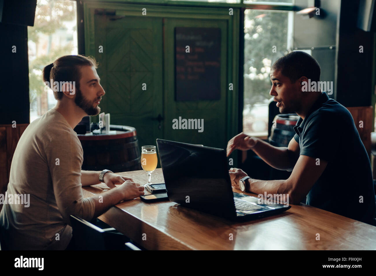 Zwei Männer mit Laptop sitzen in einer Bar im Gespräch Stockfoto