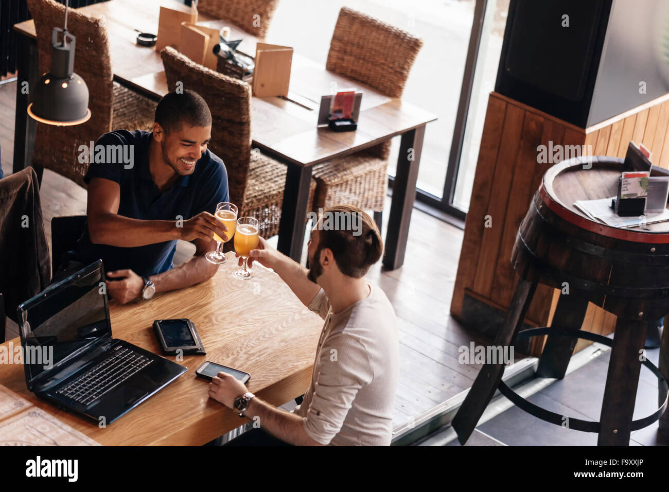 Zwei Männer mit Laptop und tragbare Geräte in einer Bar klirrendes Biergläser Stockfoto