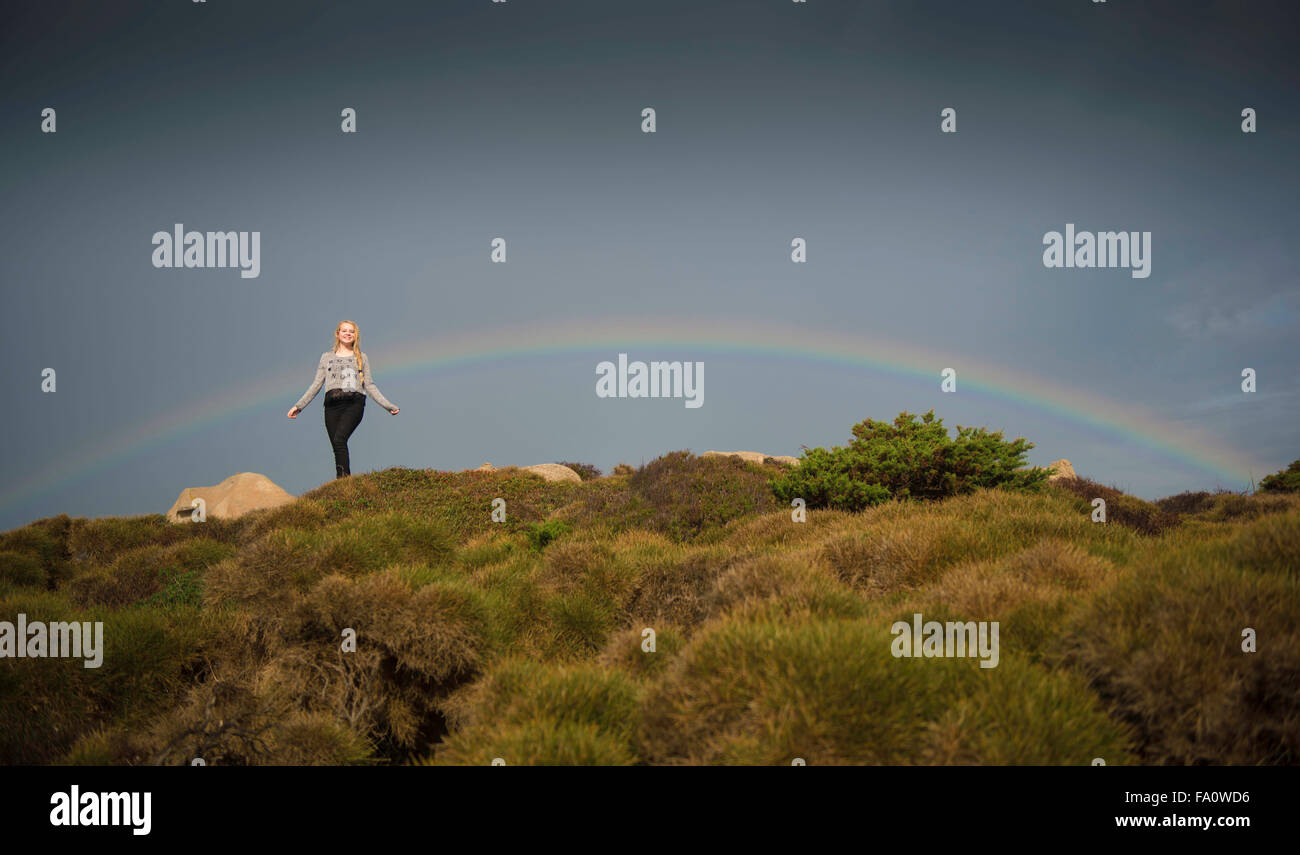ein junges Mädchen auf einem Hügel mit einem Regenbogen hinter ihr Stockfoto