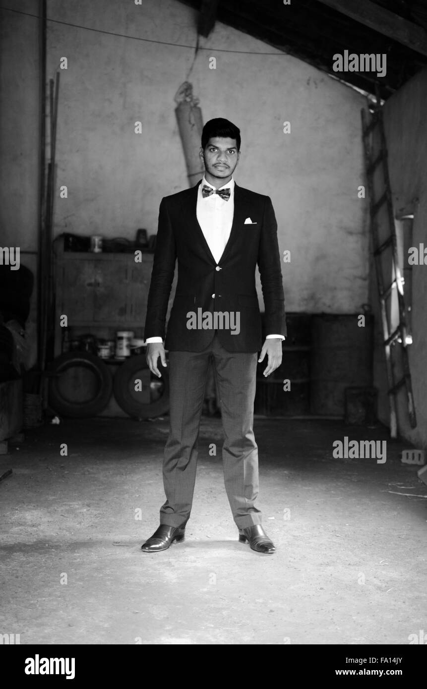 Schwarz-weiß-Porträt eines jungen indischen Mannes gekleidet im schwarzen Anzug stehen in einer alten Garage Zimmer. Stockfoto