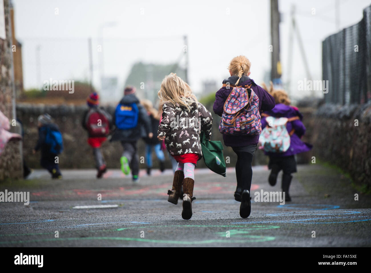 Eine Gruppe von primären Schulkinder schneidigen Rauschen läuft aus ihrer kleinen Landschule am Ende des Tages zu Beginn des Urlaubs am Wochenende oder an Feiertagen. Wales UK Stockfoto