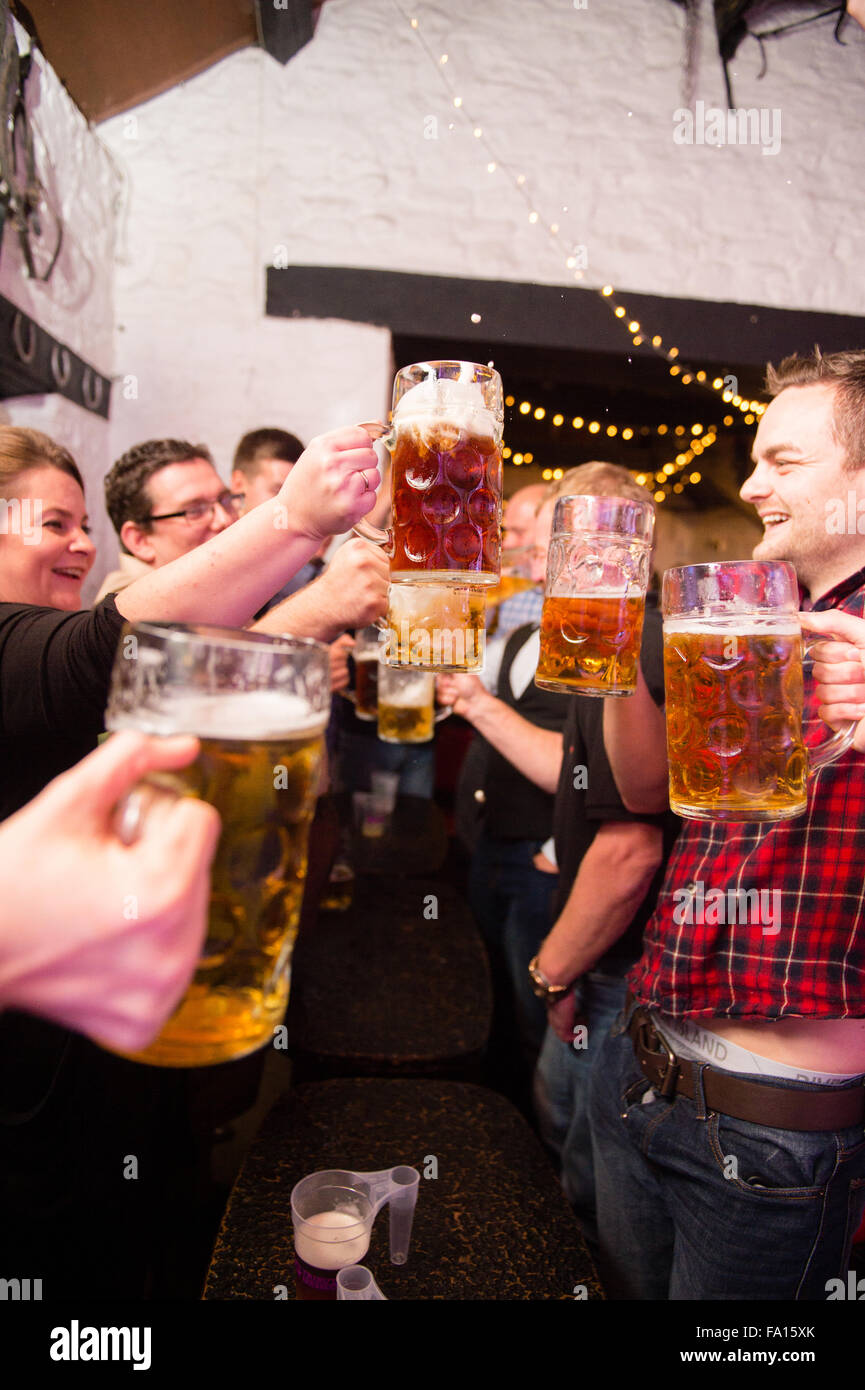 Eine Gruppe von Männern und Frauen Spaß amüsieren sich Bier trinken und Lager aus Glas "Bierkrüge" bei einer deutschen Themen Bavarian Stompers Party-Nacht in einer Kneipe, Wales UK Stockfoto