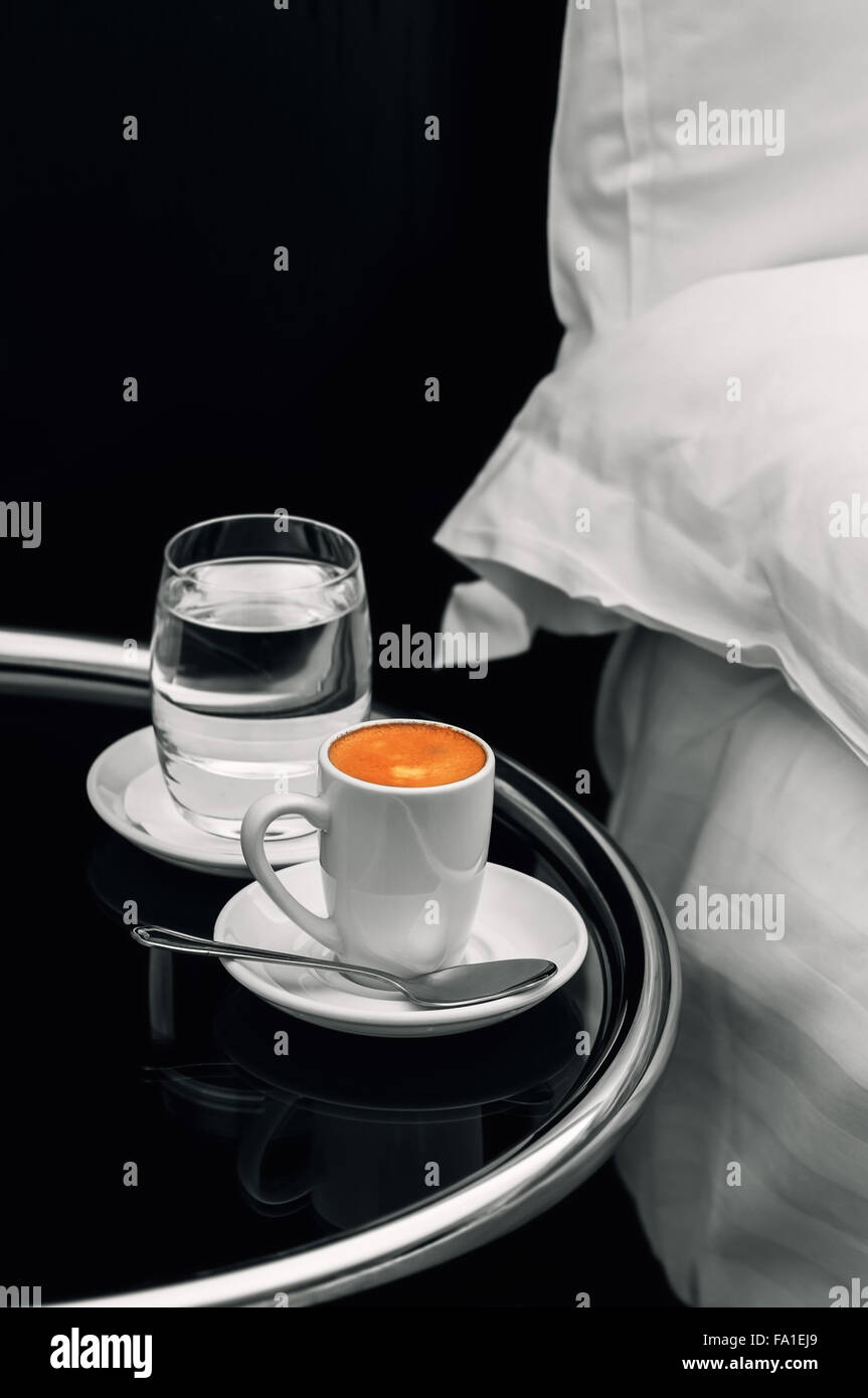 Volle Tasse Espresso-Kaffeemaschine und ein Glas Wasser auf den Nachttisch closeup Stockfoto