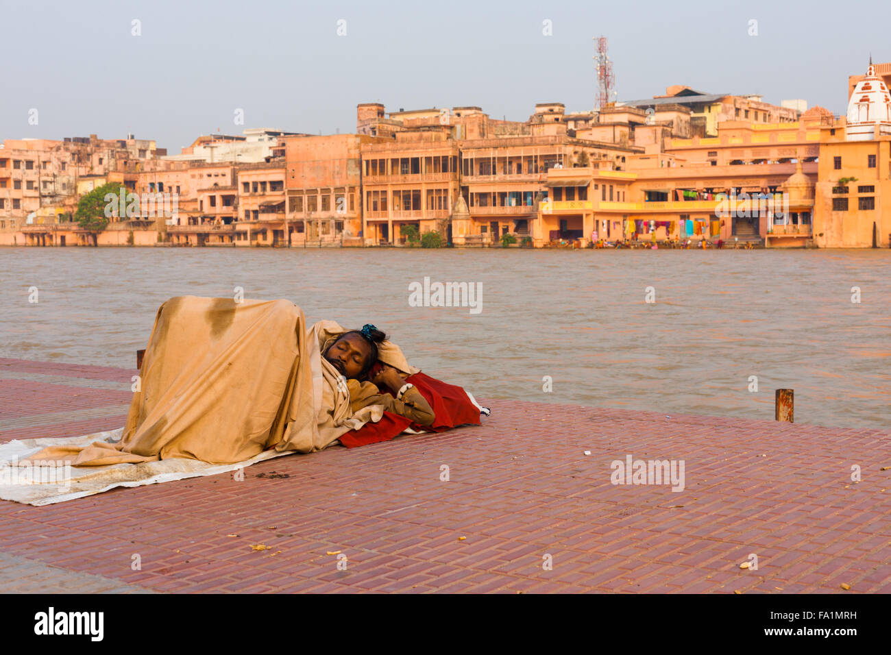 Ein indischer Obdachloser schlafen auf harten Fußweg unter Decke neben dem Ganges Fluss Rand Stockfoto