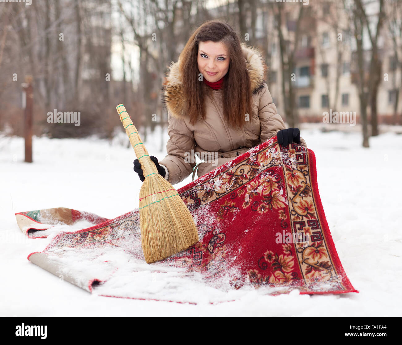 Lächelnde Frau reinigt Teppich mit Schnee im Wintertag Stockfoto