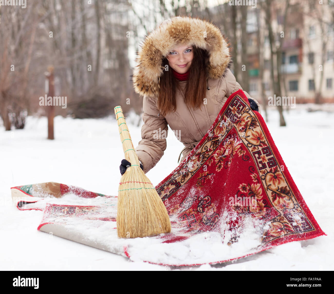 Lächelnde Frau reinigt Teppich mit Schnee im winter Stockfoto
