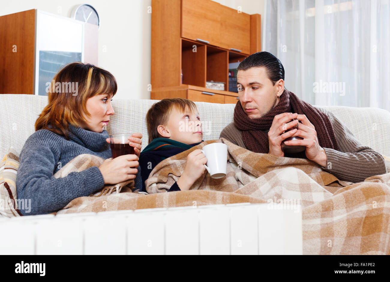 Einfrieren von Eltern und Sohn im Teenageralter Erwärmung in der Nähe von warme Heizung im Haus Stockfoto