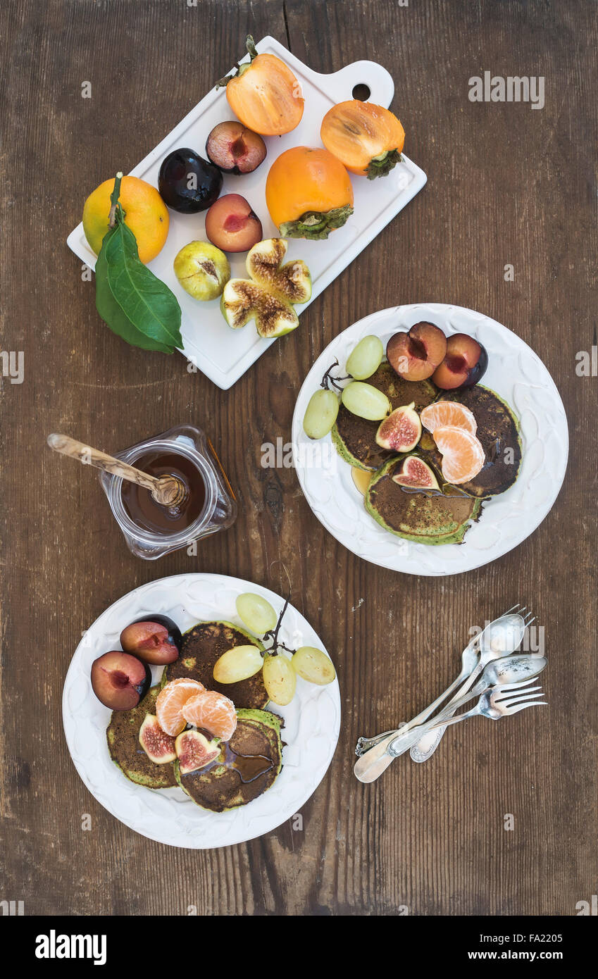 Frühstücks-Set. Selbstgemachte Zucchini-Pfannkuchen mit frischen Pflaumen, Mandarinen, Trauben, Feigen und Honig in den weißen keramischen Platten über rustikal Stockfoto