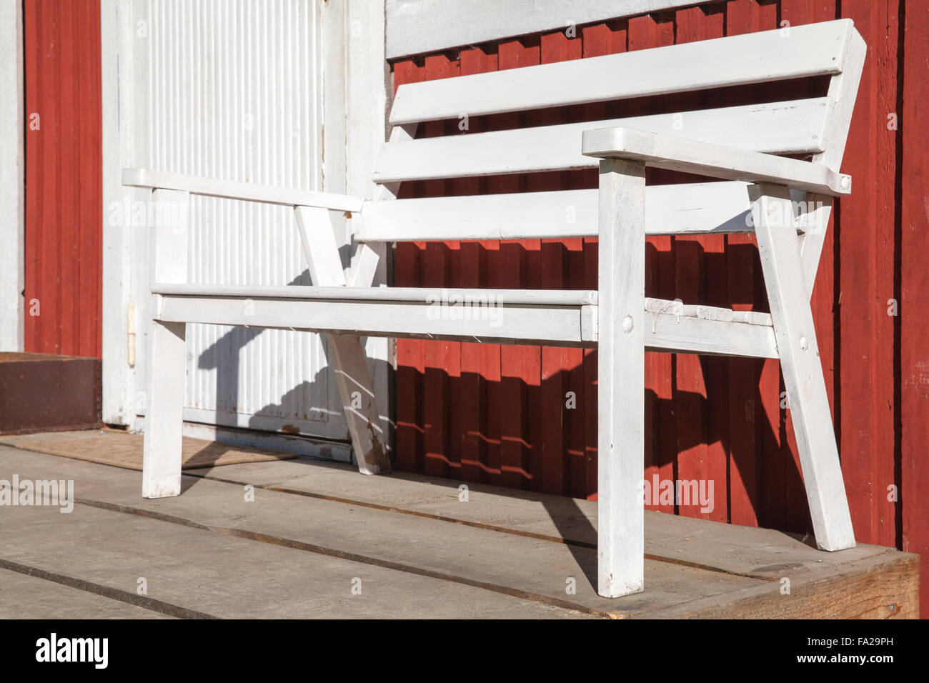 Weiße Holzbank steht auf der Terrasse des skandinavischen roten Holzhaus Stockfoto