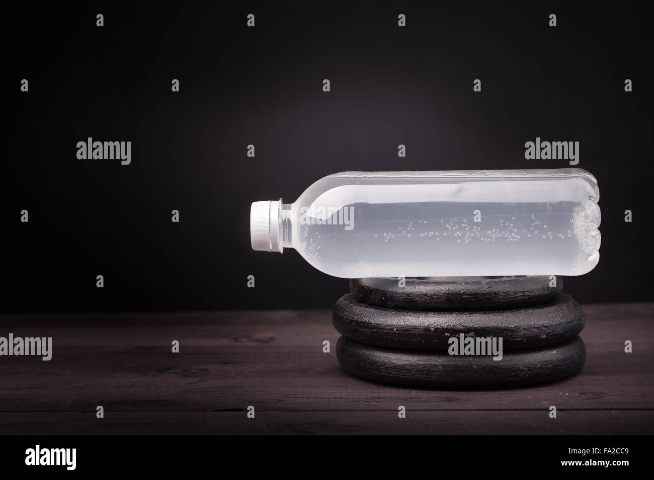 Sportgeräte. Wasserflasche und Hantel Gewichte an einem schwarzen Holztisch und Hintergrund mit Textfreiraum Stockfoto