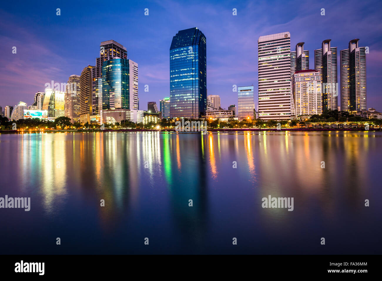Moderne Wolkenkratzer und Lake Rajada in der Nacht, im Benjakiti Park in Bangkok, Thailand. Stockfoto