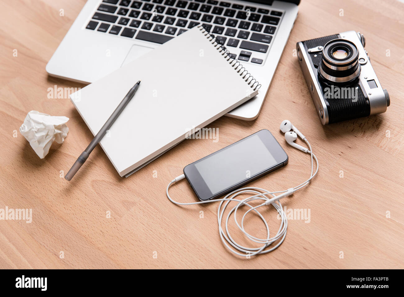 Laptop, Vintage-Kamera, Handy mit Kopfhörer und Notizbuch mit Stift auf Holztisch liegend Stockfoto