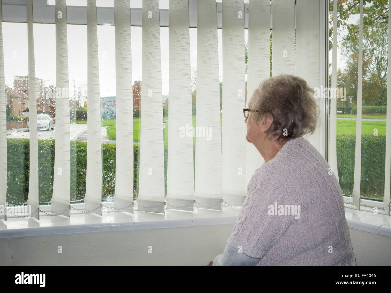 90 Jahre alte Frau Blick aus Fenster an einem regnerischen Tag. UK Stockfoto
