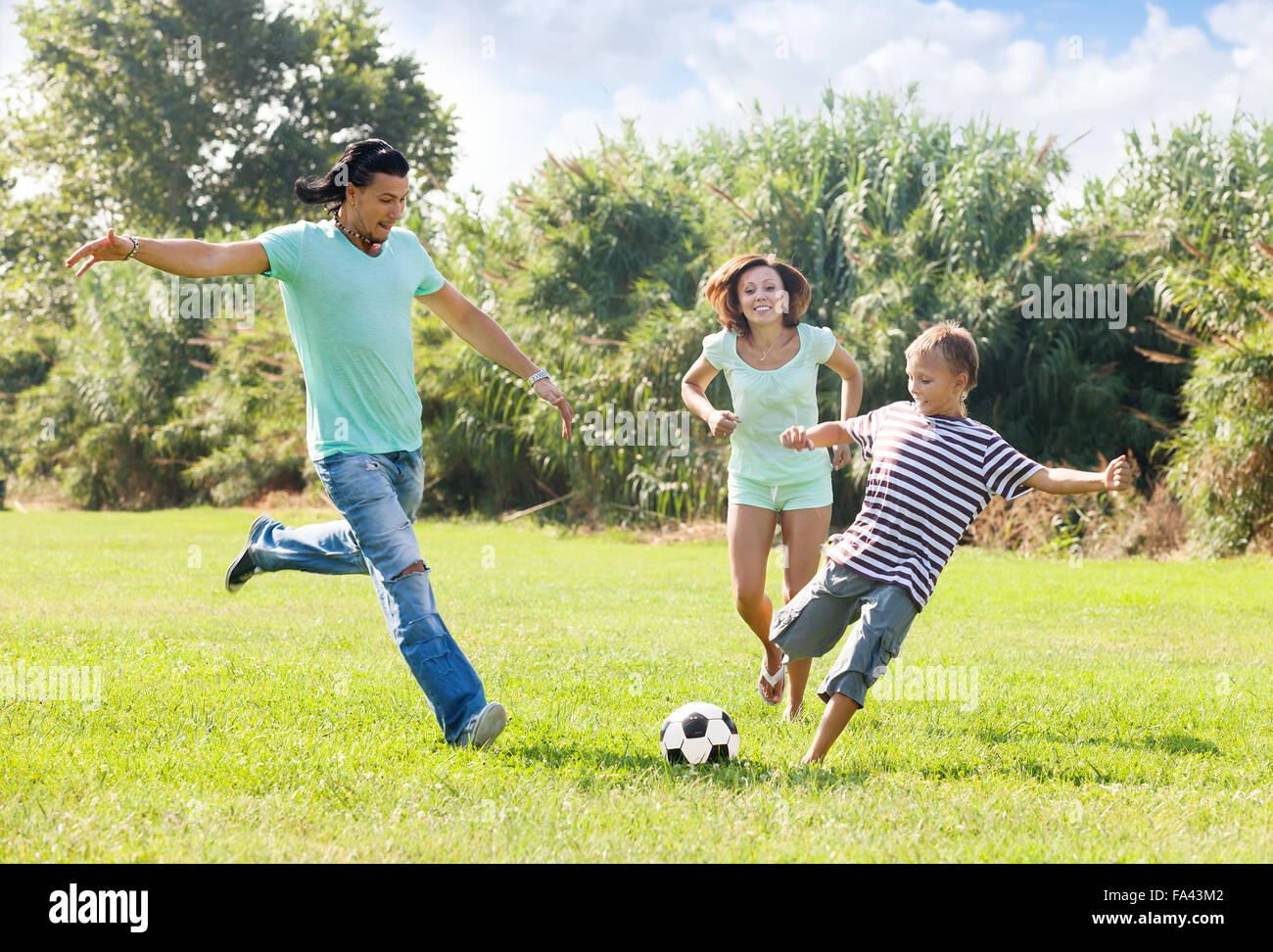 Paar mittleren Alters mit Sohn spielen mit Fußball im Sommerpark Stockfoto