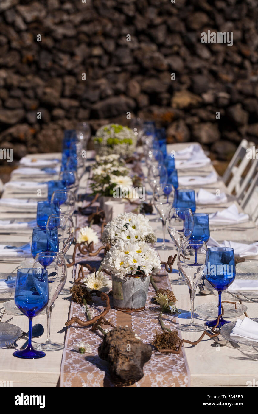 Weißen Tisch und hölzerne Stühle set mit blauen Gläsern, Blumen und Dekorationen für eine Feier im Freien. Stockfoto