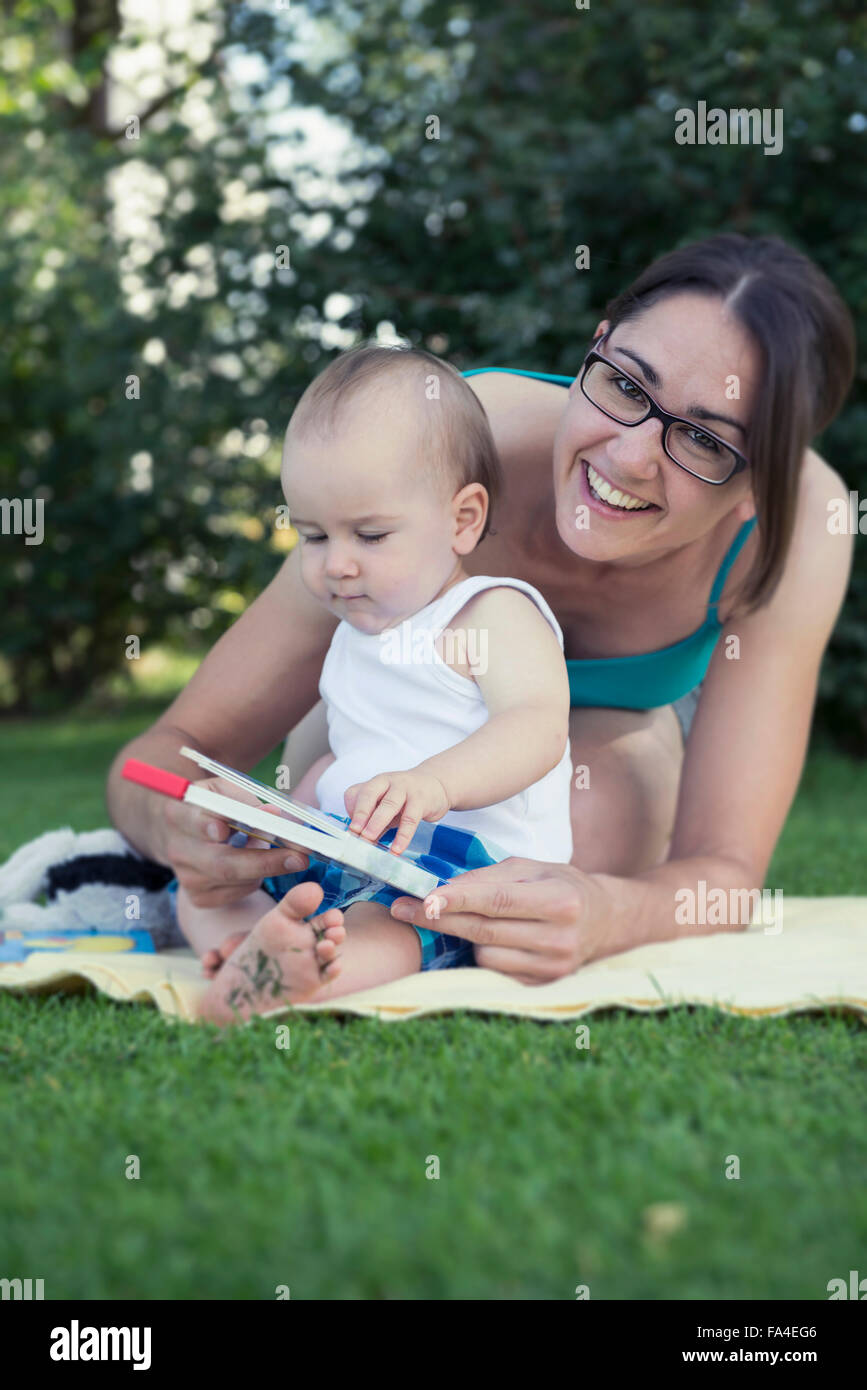 Mutter und Baby Boy hält ein Bilderbuch und lachend in Rasen, München, Bayern, Deutschland Stockfoto