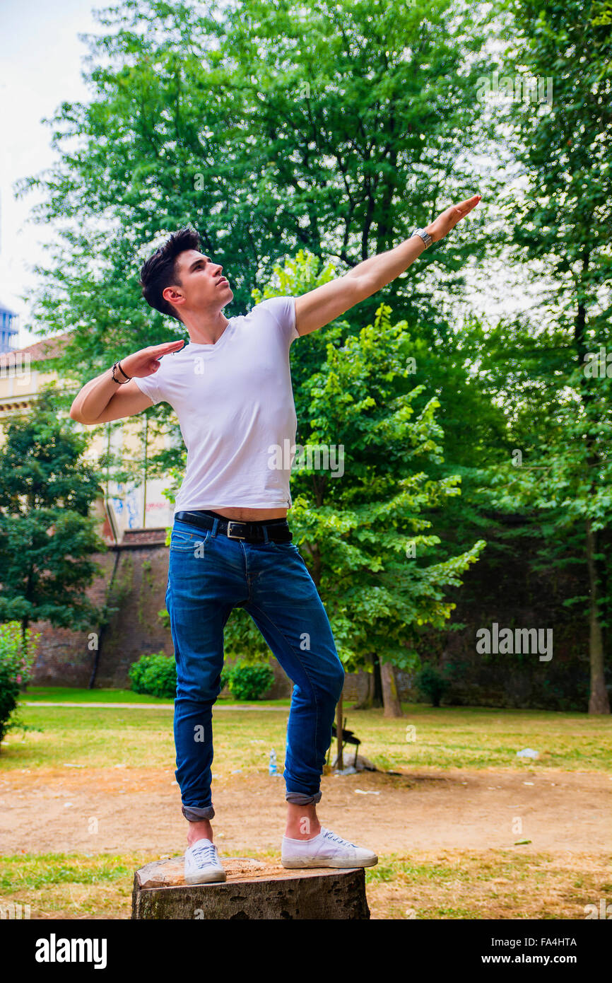 Seitenansicht des jungen Mann posiert auf Baumstumpf Statue zu imitieren Stockfoto