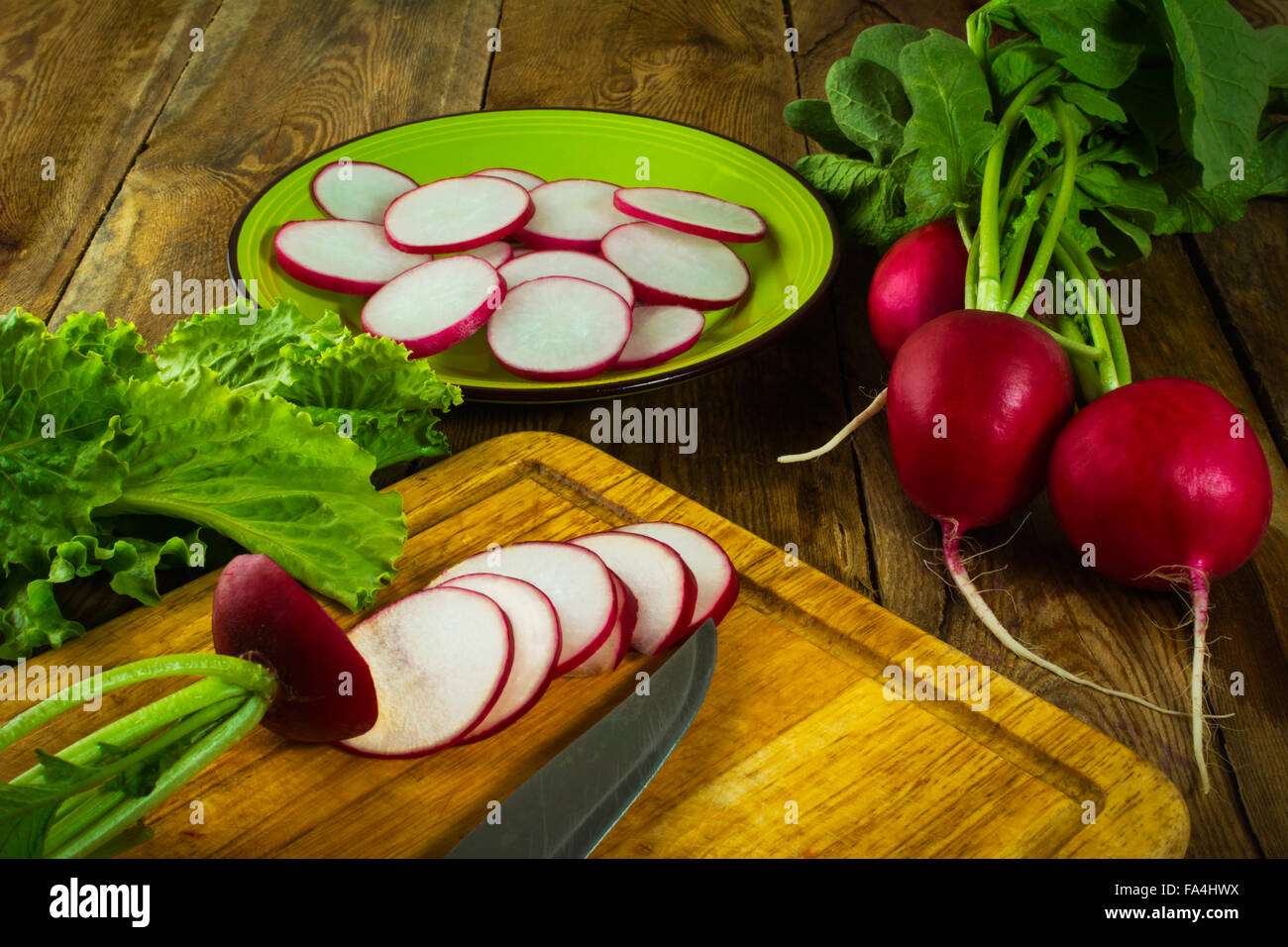 Eine Handvoll frische Radieschen, Salatblätter, Scheiben von Rettich und Messer auf alten Schneidebrett Stockfoto