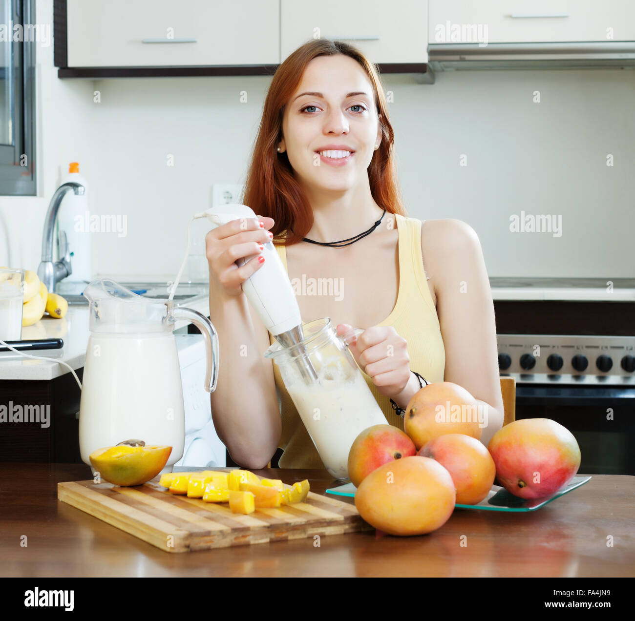 gewöhnliche Frau, die Zubereitung von Getränken mit Blender von Mango und Milch in der heimischen Küche Stockfoto