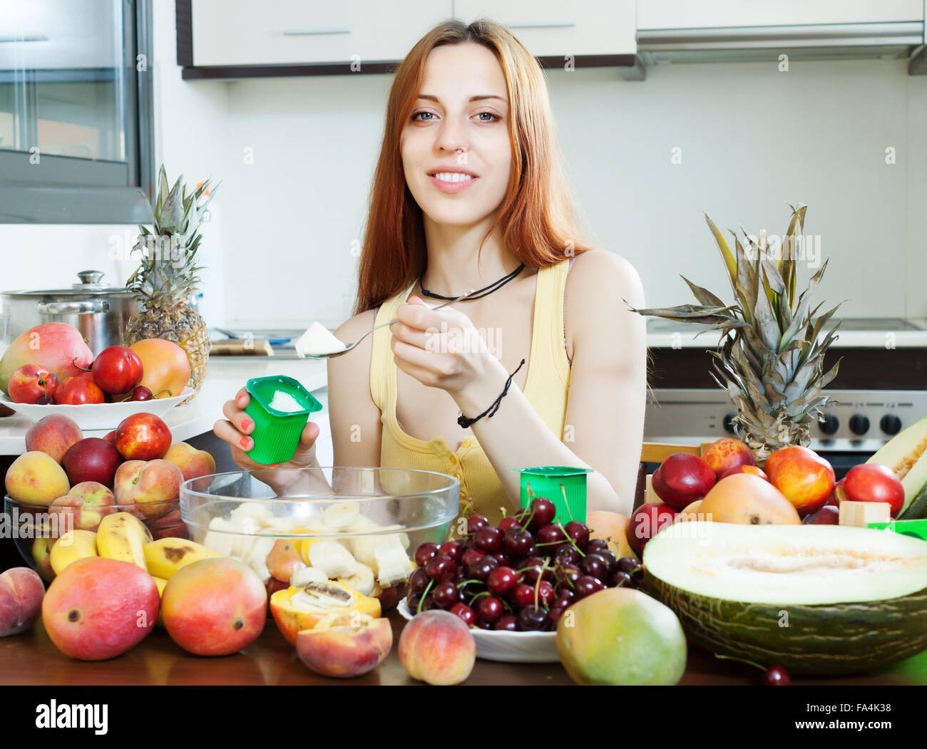 Positiven langhaarige Frau macht Obstsalat mit Joghurt in der Küche zu Hause Stockfoto